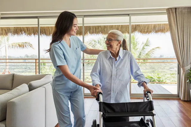 Nurse helping an elderly woman walk with a walker inside a bright Bali villa