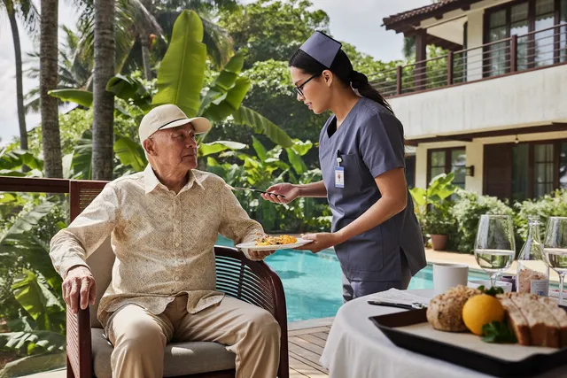 Live-in nurse sharing morning tea with an elderly man on a Bali villa terrace